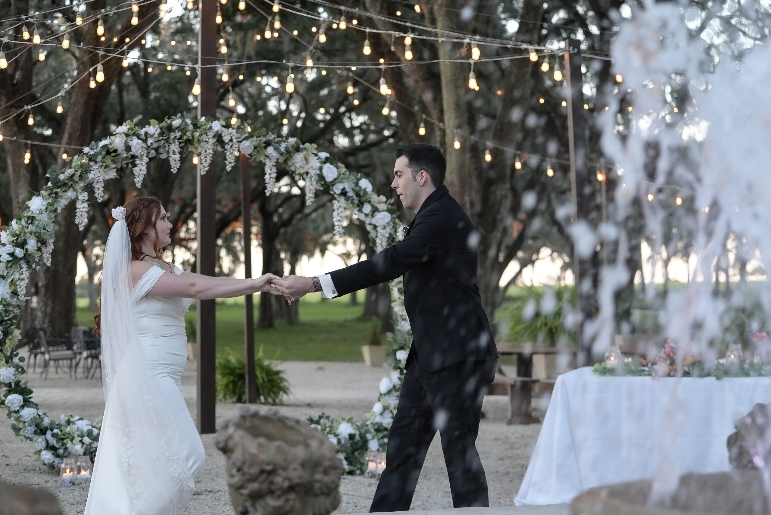 Bride and groom dancing outdoors at wedding reception with string lights.